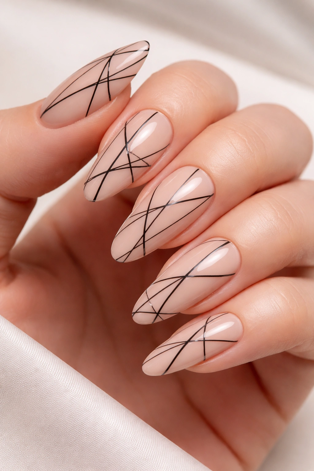 Close-up of long nude oval nails with black geometric line art.