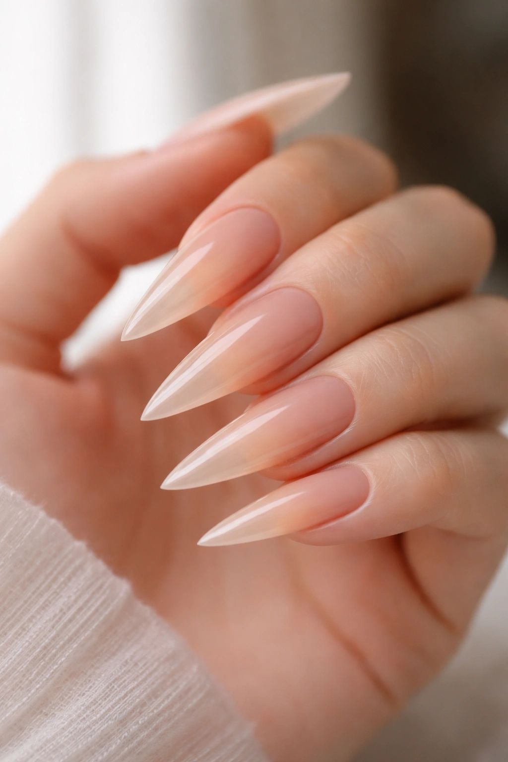 Close-up of nude-to-clear gradient on long stiletto nails with a bare hand