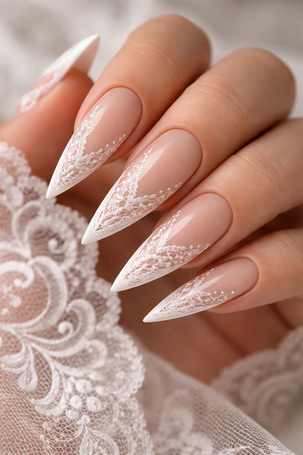 Close-up of nude base stiletto nails with white lace patterns