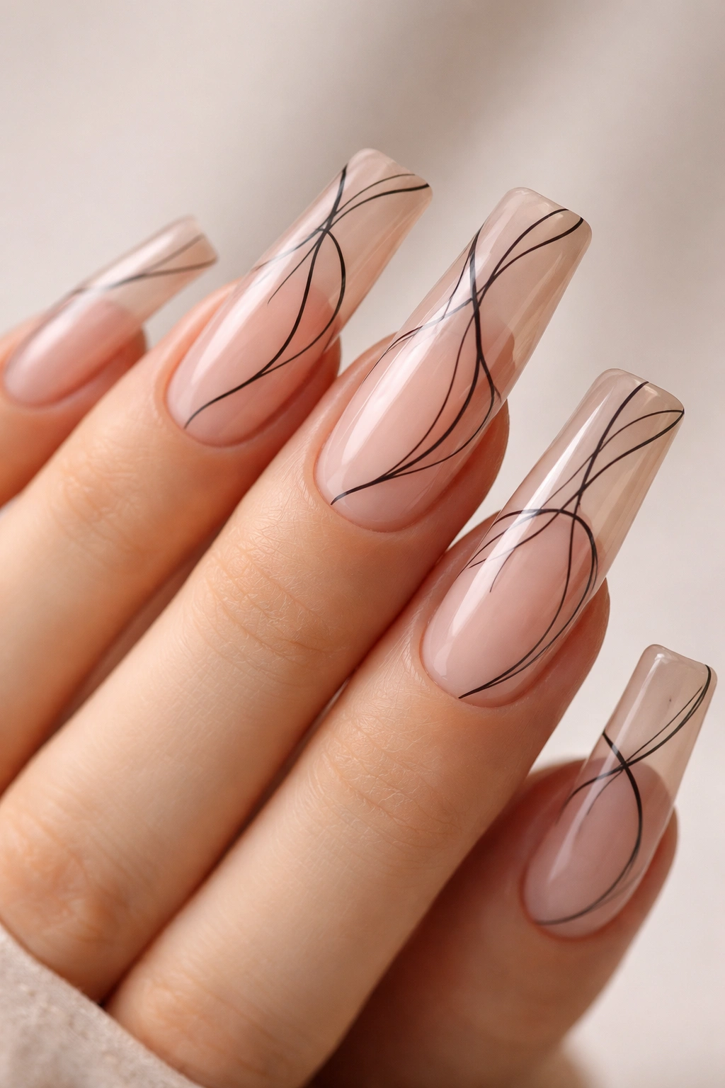 Sheer nude nails with black line art on long nails.