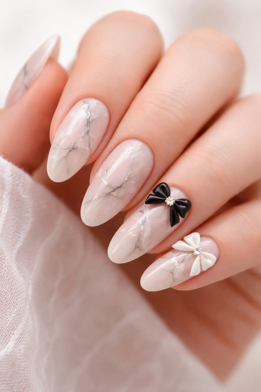 Nude nails with delicate marble texture and bow accents on selected nails.