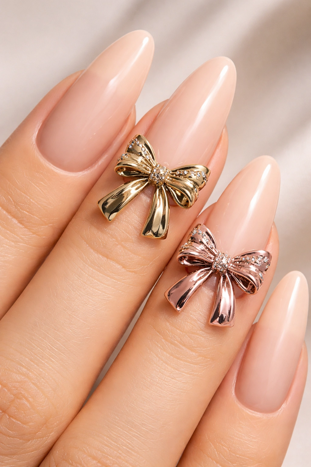 Close-up of nude nails with oversized metallic 3D bows on two nails.
