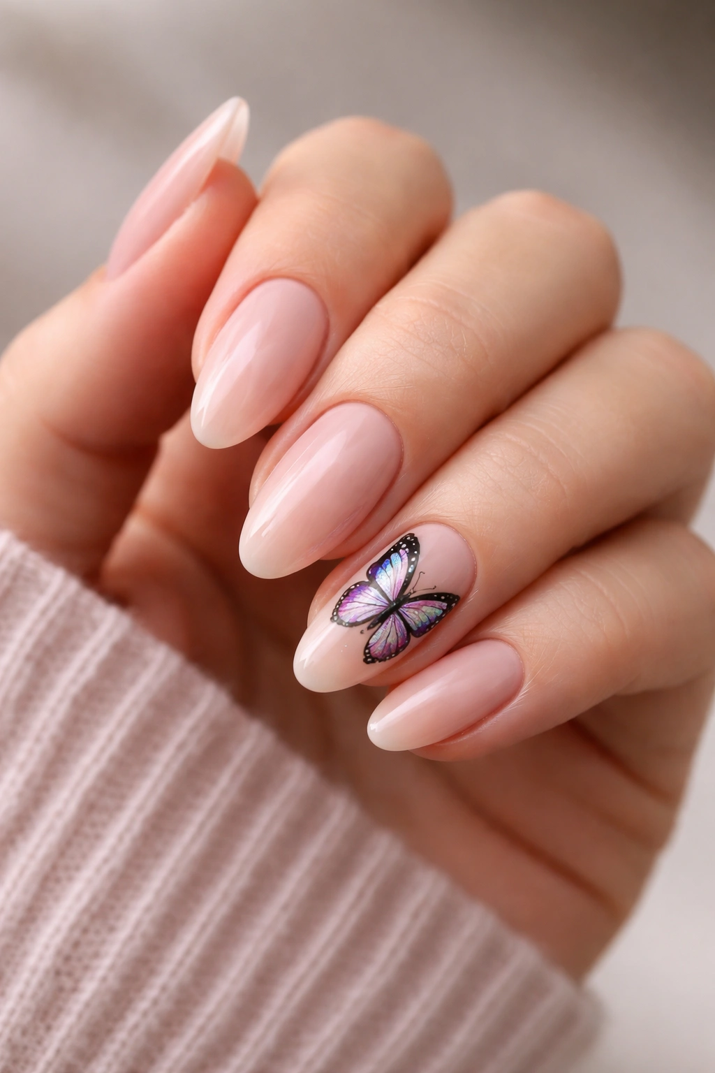 Nude almond nails with one large butterfly accent nail on ring finger