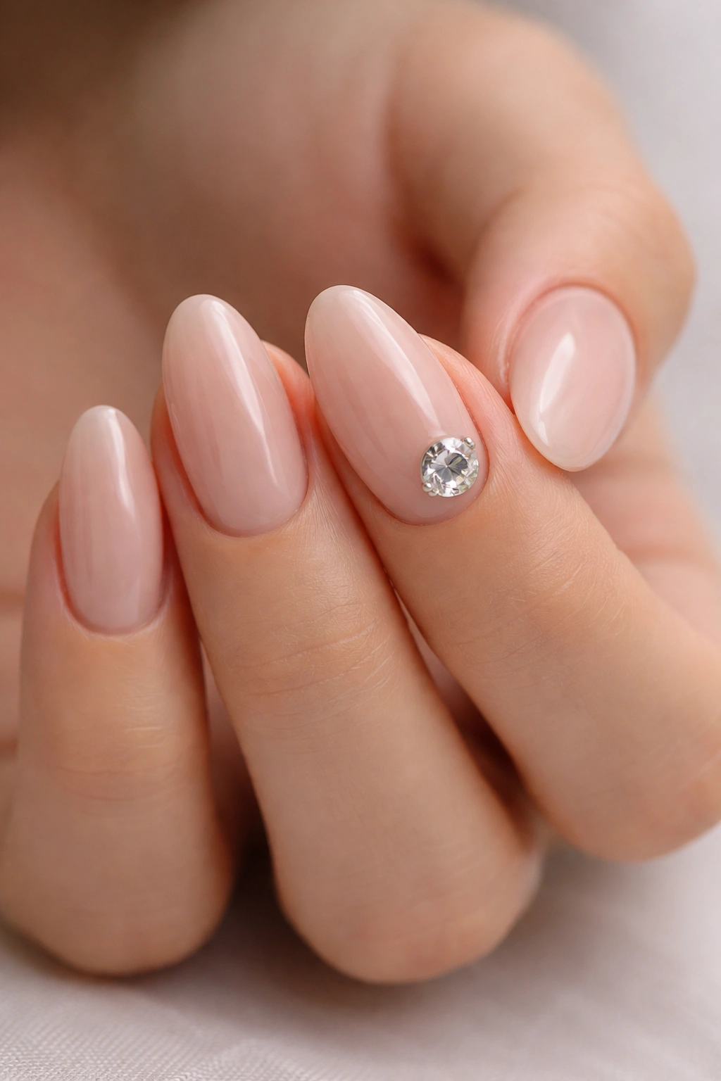 Close-up of nude almond nails with a single oversized gem
