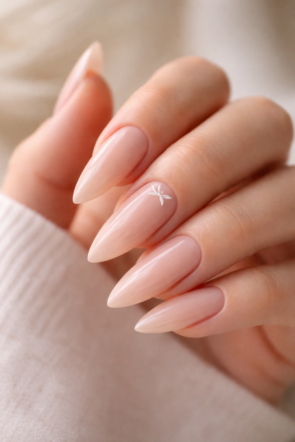 Nude stiletto nails featuring a single minimalist bow at the base