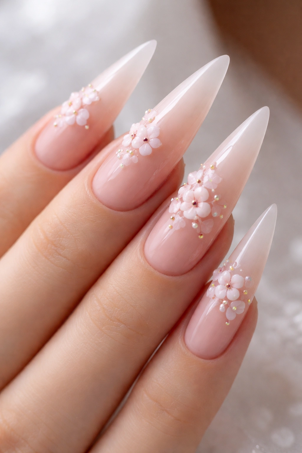 Close-up sheer nude stiletto nails with delicate raised cherry blossoms