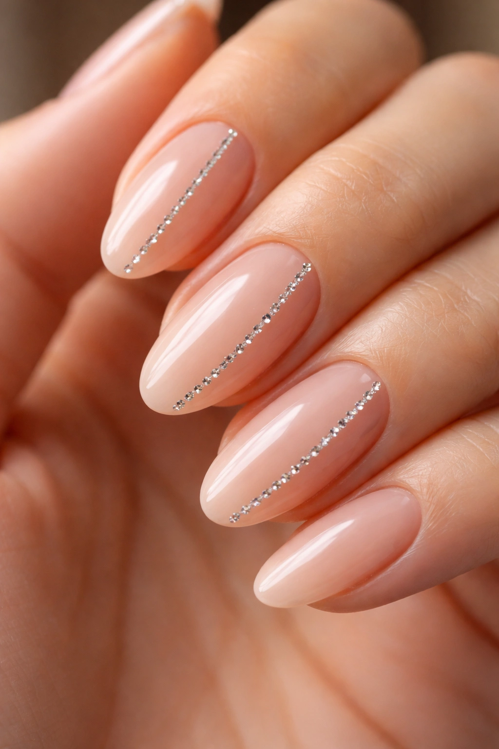 Close-up of bare nude almond nails with a single crystal line along one edge