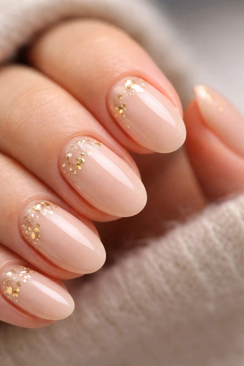 Nude short oval nails with scattered gold foil flecks on neutral background