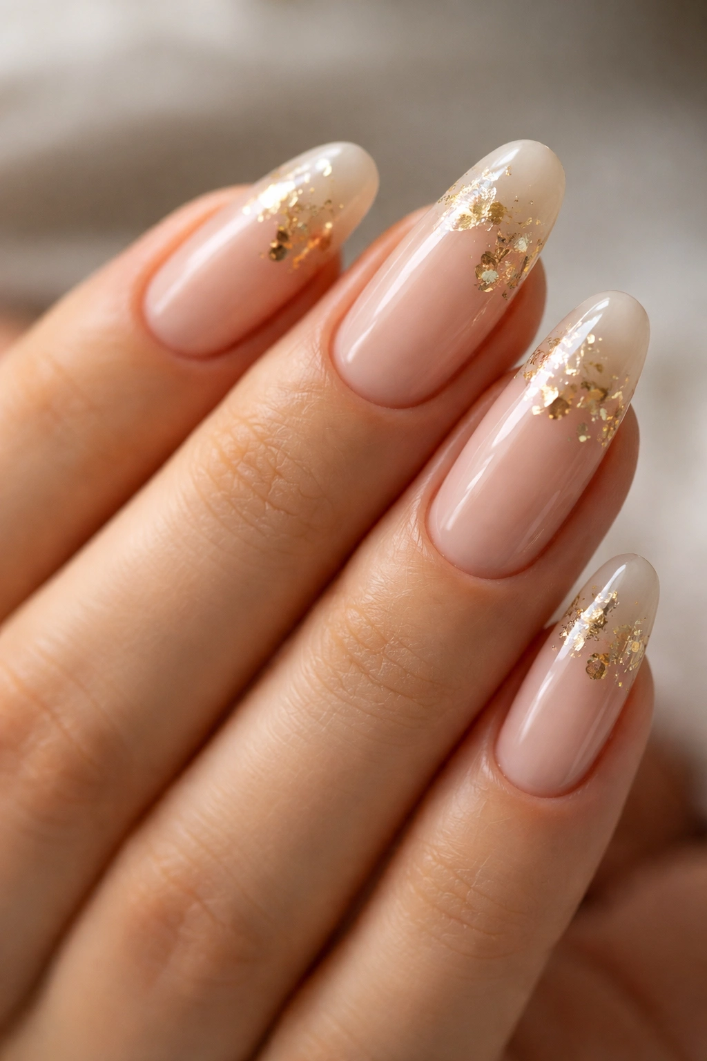 Close-up of nude oval acrylic nails with gold foil near cuticle