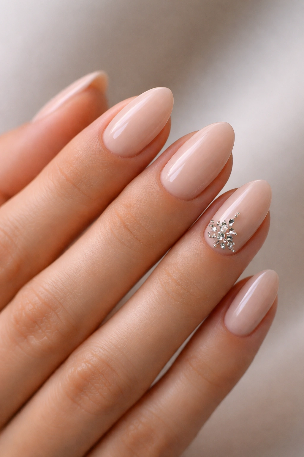 Nude almond nails with gemmed ring finger accent cluster