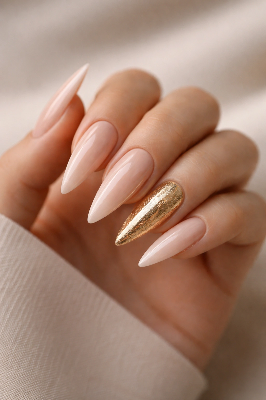 Close-up of nude-based stiletto nails with a single gold accent nail on a hand.