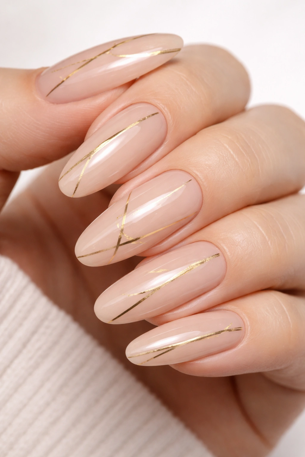 Close-up of nude nails with thin gold stripes on long oval shape.