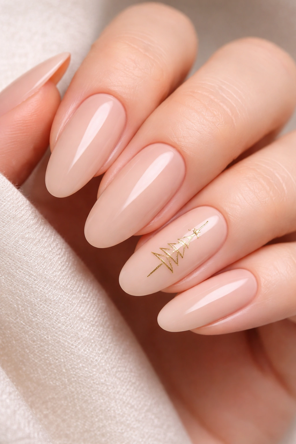 Close-up of nude long oval nails with a minimalist gold Christmas tree on the accent nail