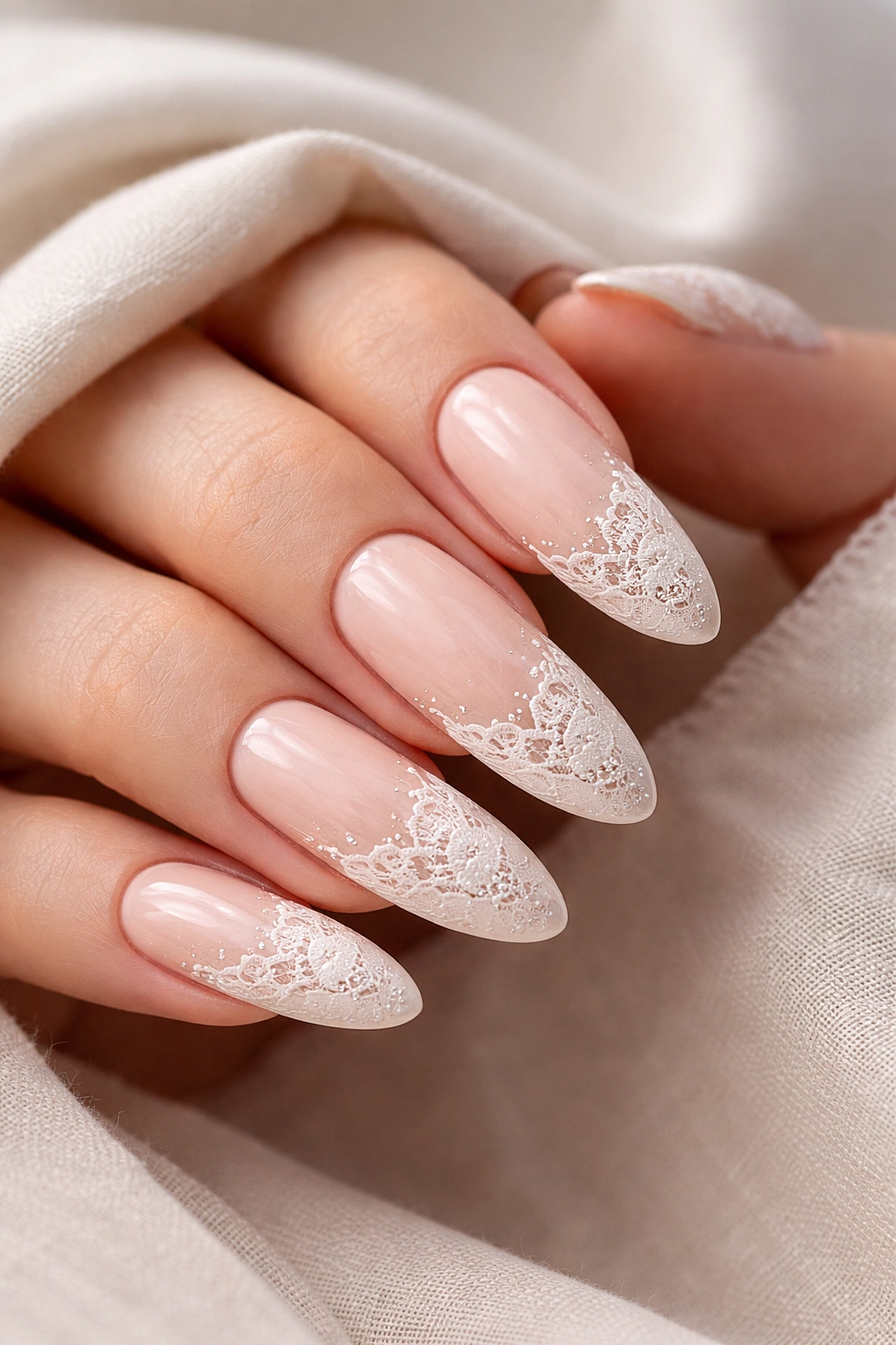 Close-up of nude nails with intricate lace design on long ovals