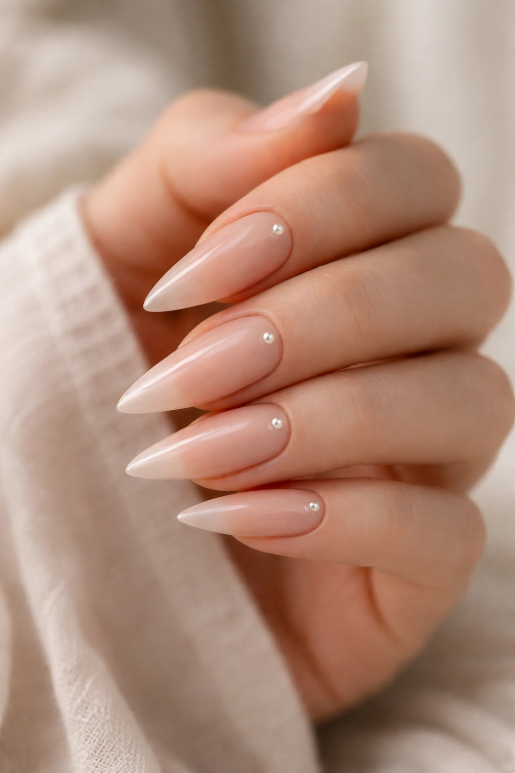 Minimal nude stiletto nails with small pearl accents.