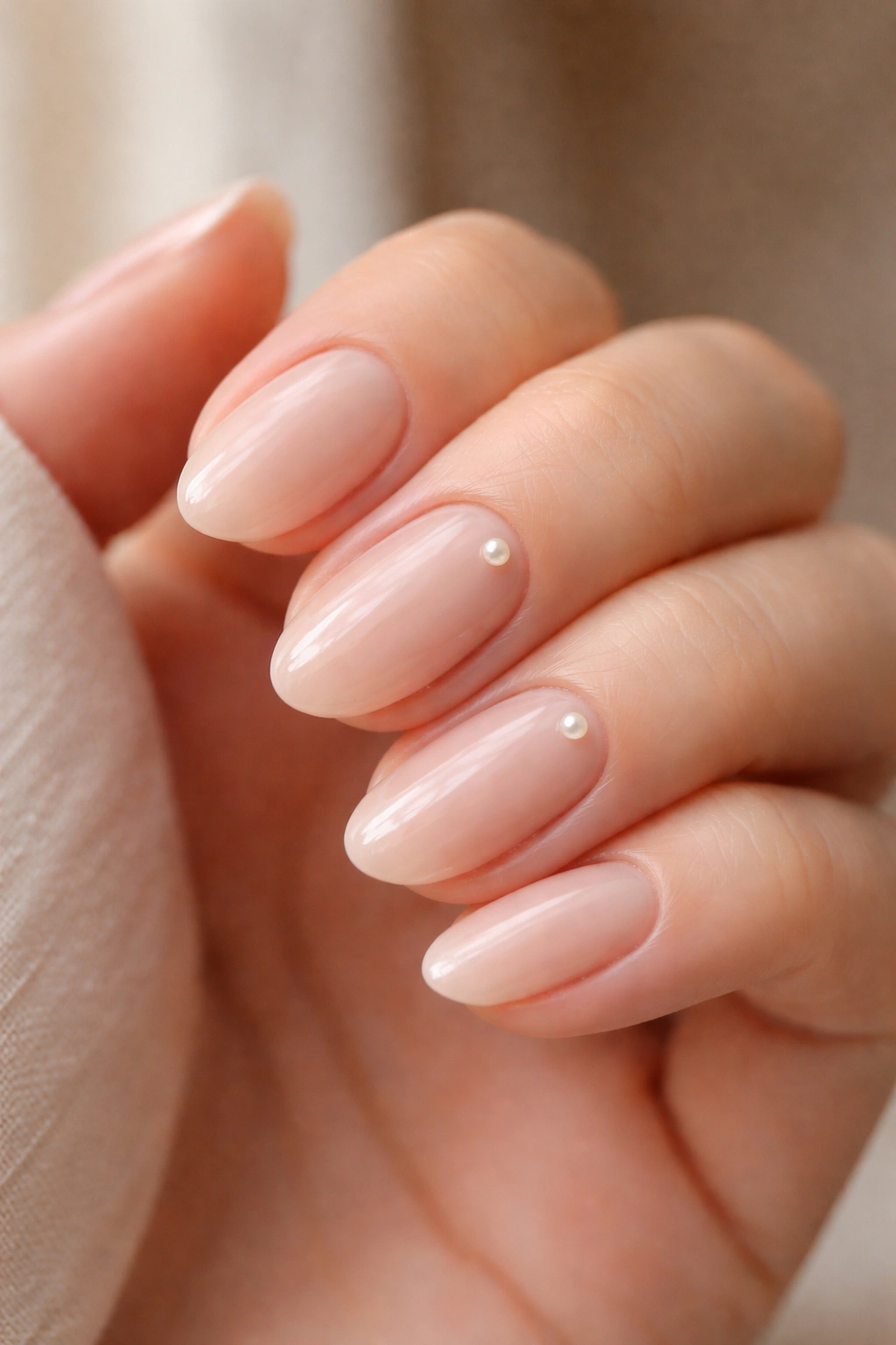 Close-up of nude short almond nails with a tiny pearl accent