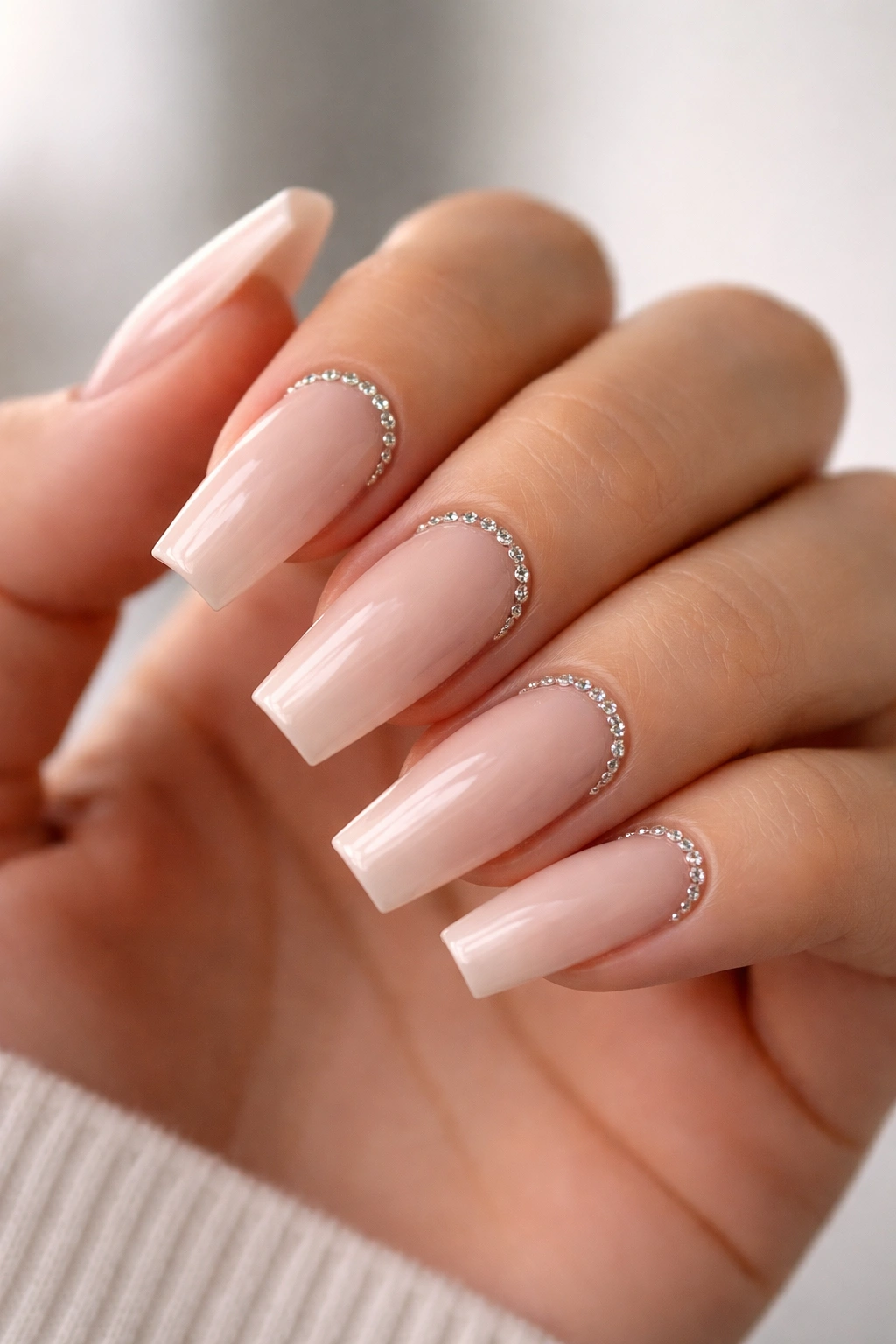 Close-up of nude coffin nails with rhinestone border along cuticles