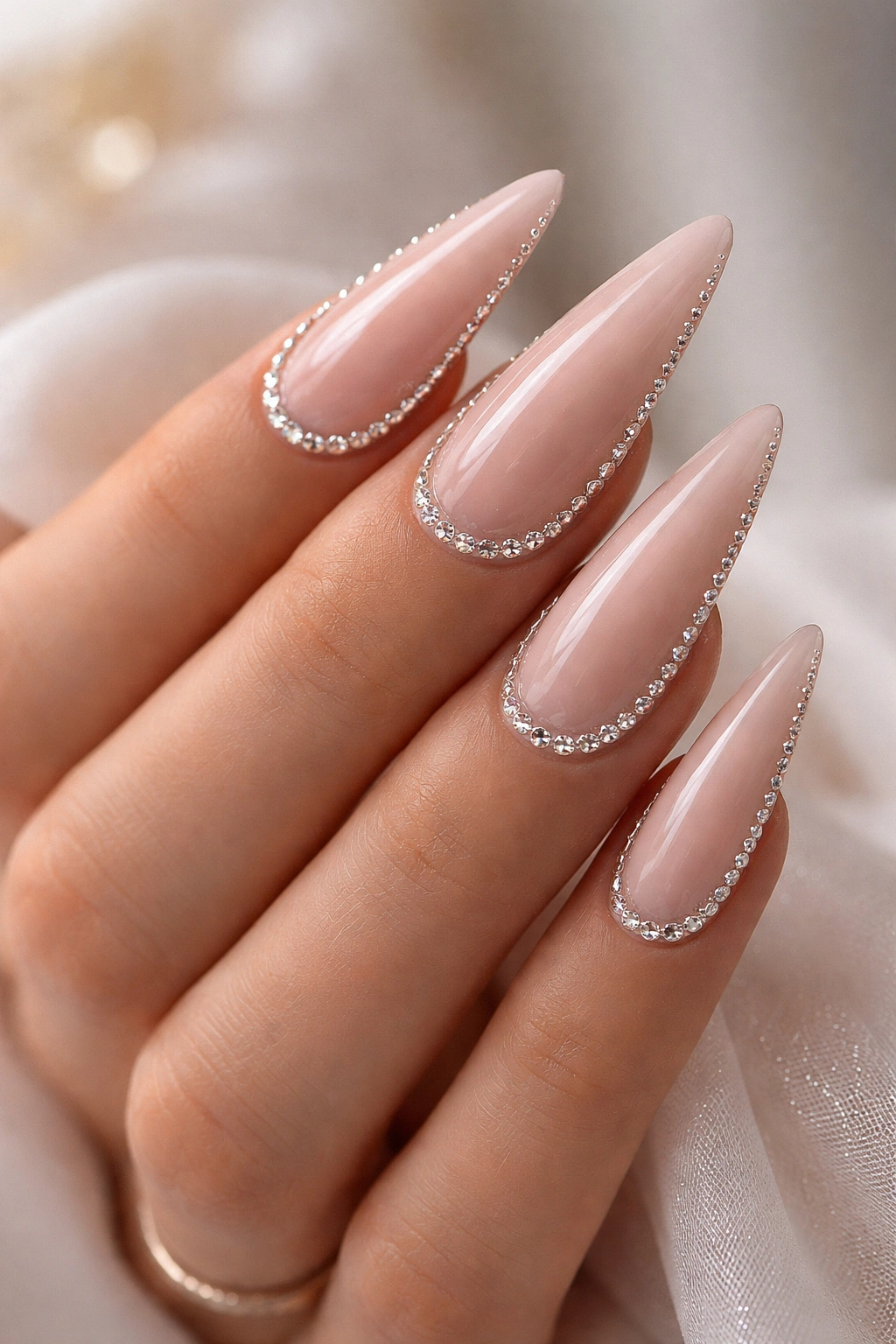 Soft nude stiletto nails with rhinestone borders along the cuticle and sides