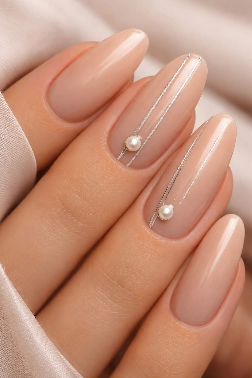 Close-up of nude long-oval nails with silver stripes and pearl accents