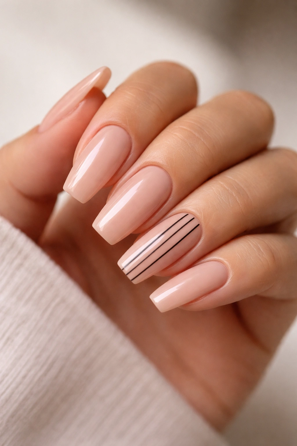 Close-up of coffin nails with nude base and thin black striped accent nails
