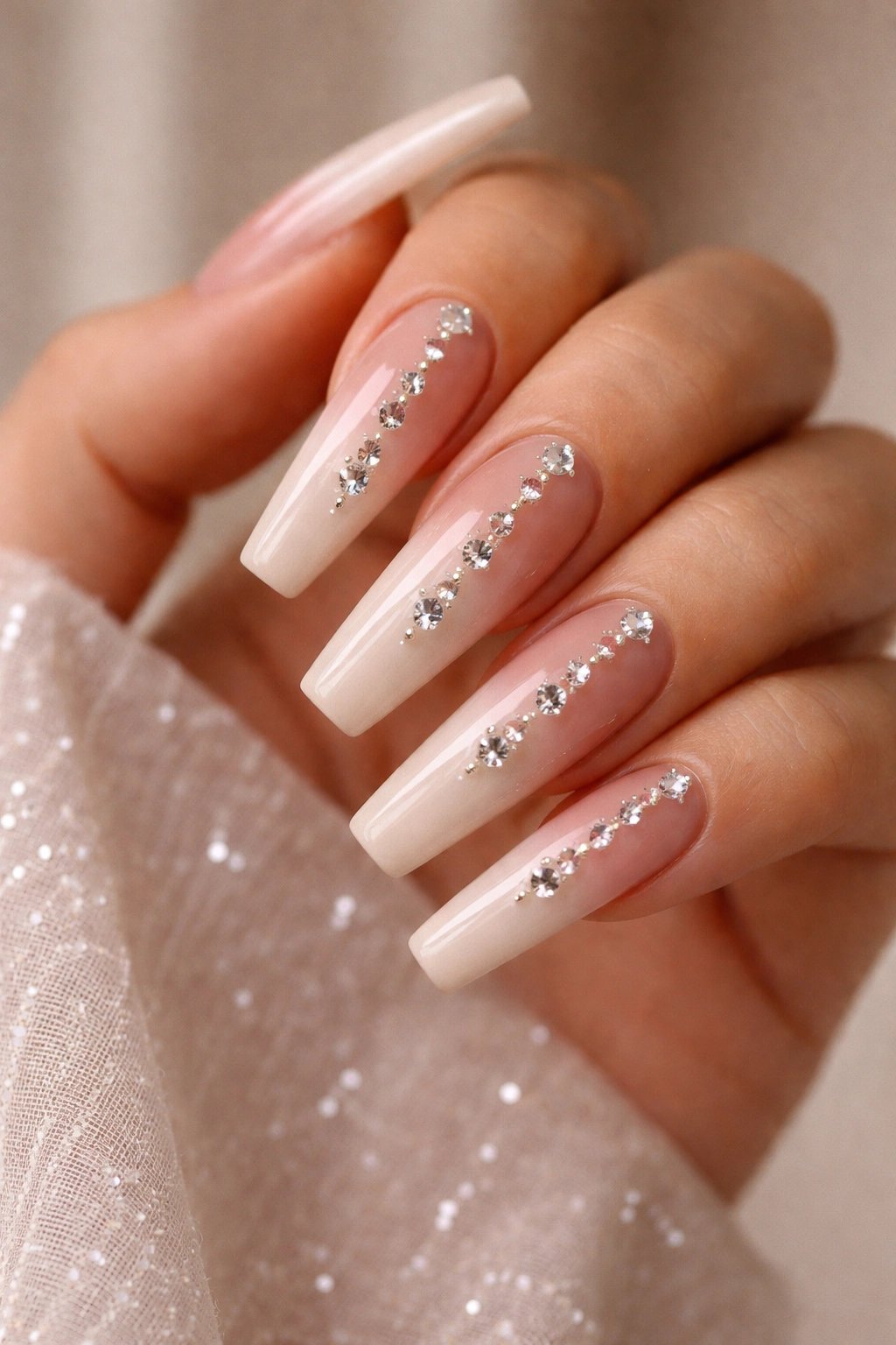 Close-up of nude ombre nails with diamond-cut crystal charms along the center