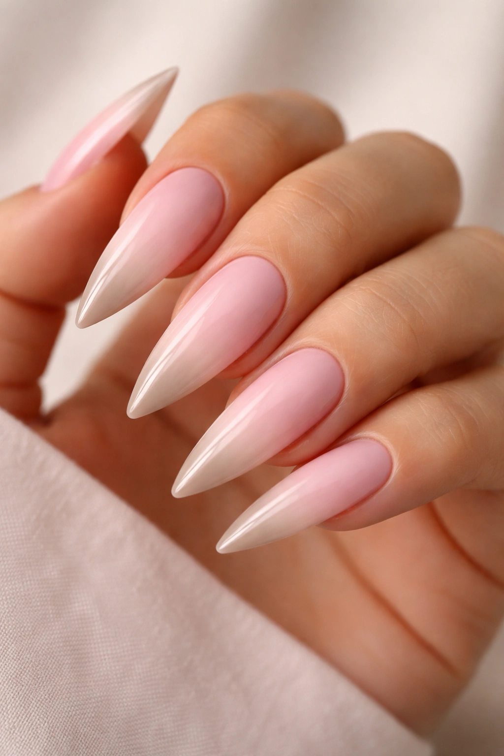 Close-up of baby pink stiletto nails with nude ombré tips on a hand
