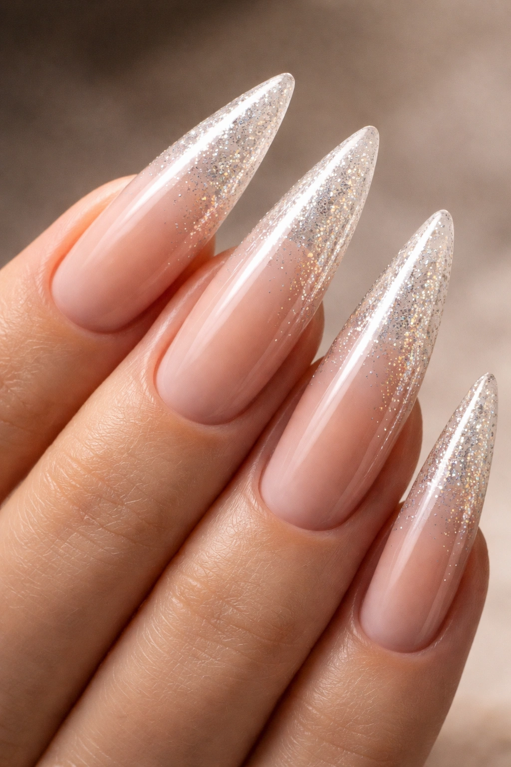 Nude ombre curved stiletto nail with sparkle fade on a neutral background