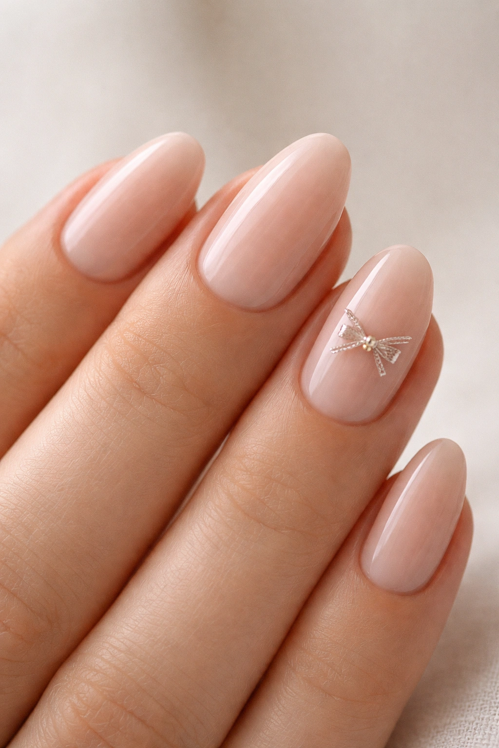 Nude pink almond nails with micro bow at cuticle on a plain background