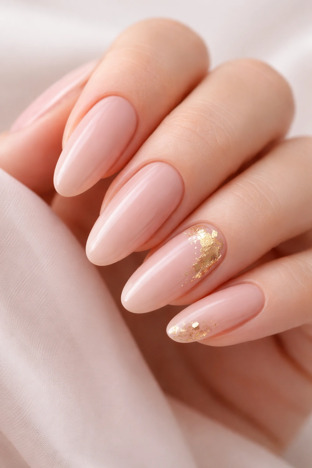 Close-up of nude pink nails with delicate gold leaf accents on ring finger