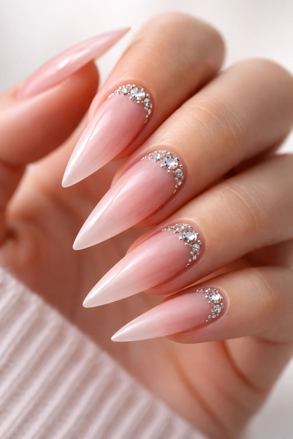Nude pink stiletto nails with rhinestones arranged along the cuticle