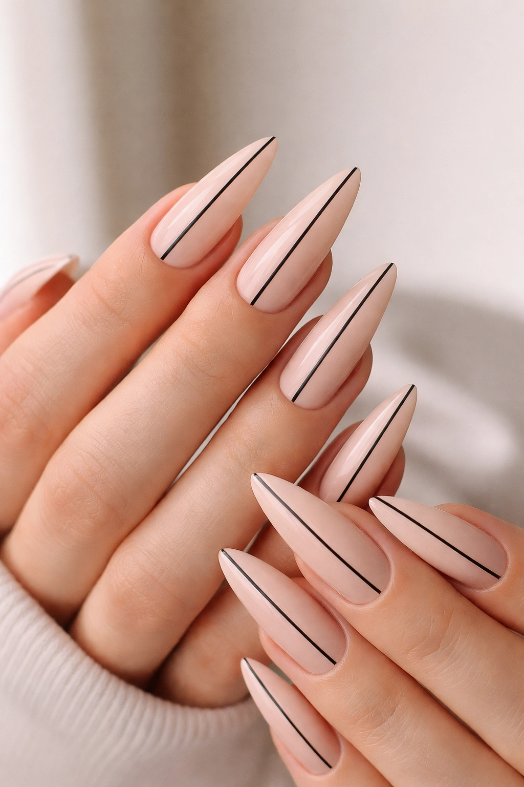 Close-up of nude stiletto nails with thin black striping tape design