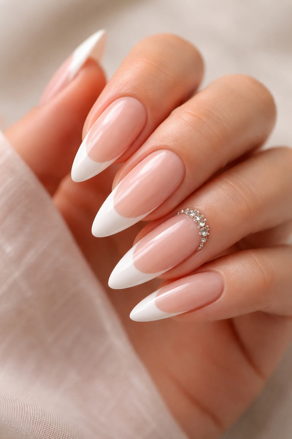 Nude and white French nails with crystal accents near the cuticle on almond nails