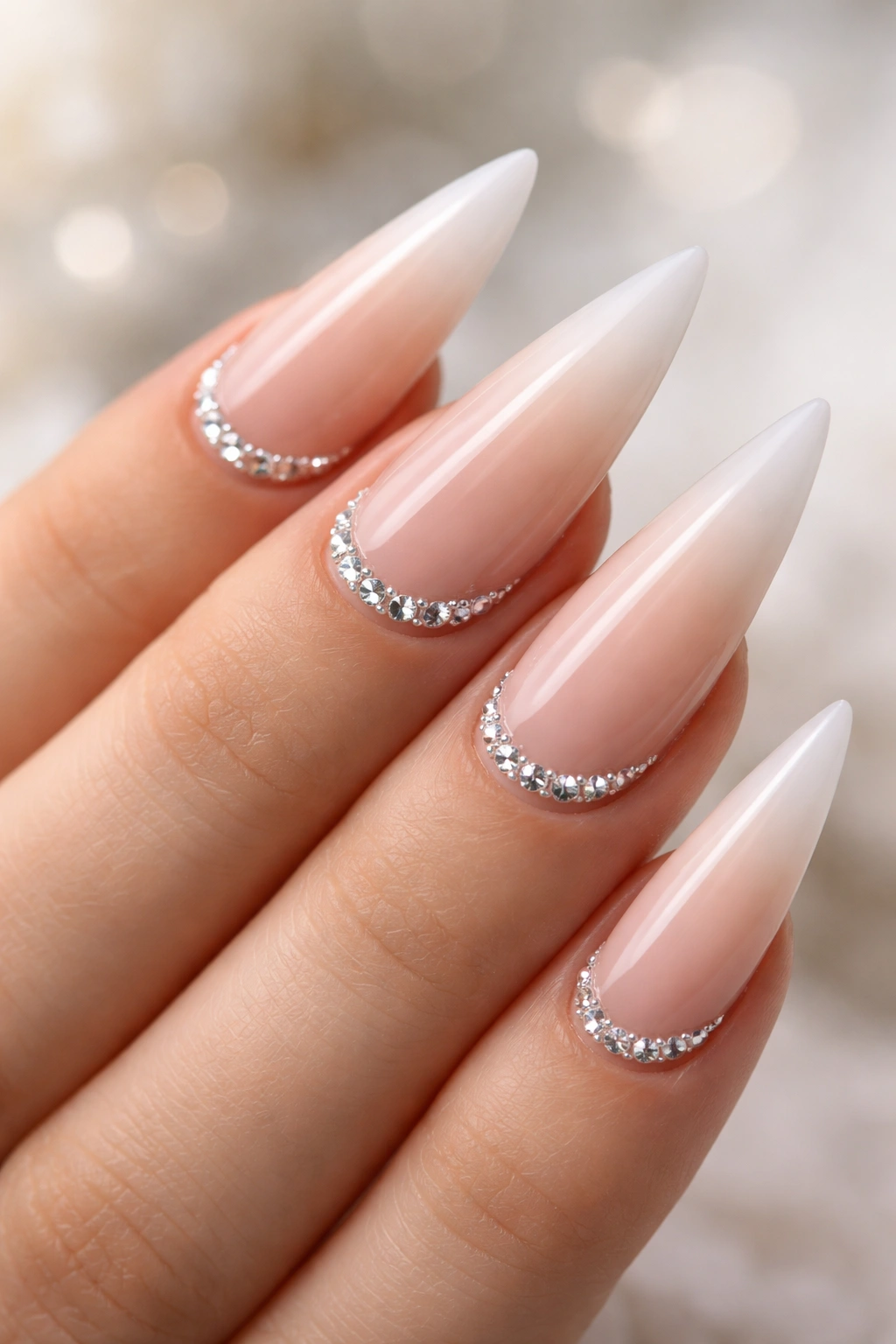 Nude to white ombre stiletto nails with rhinestone accents at the tip transition