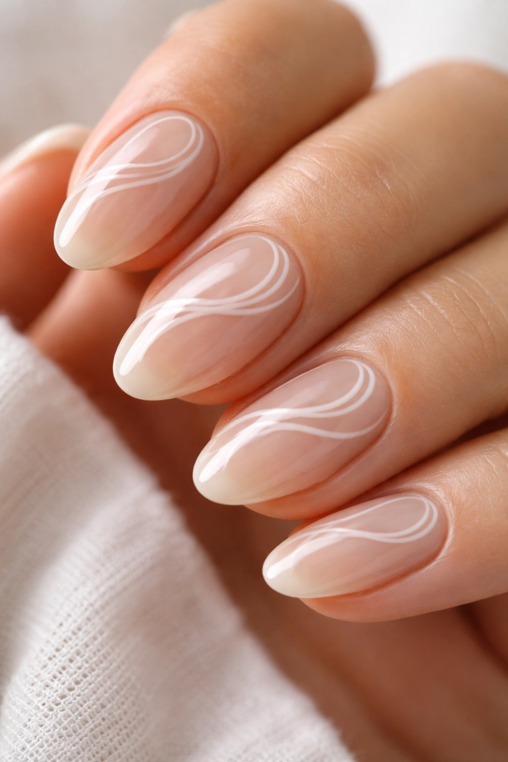 Close-up of short almond nail with nude base and white swirl art