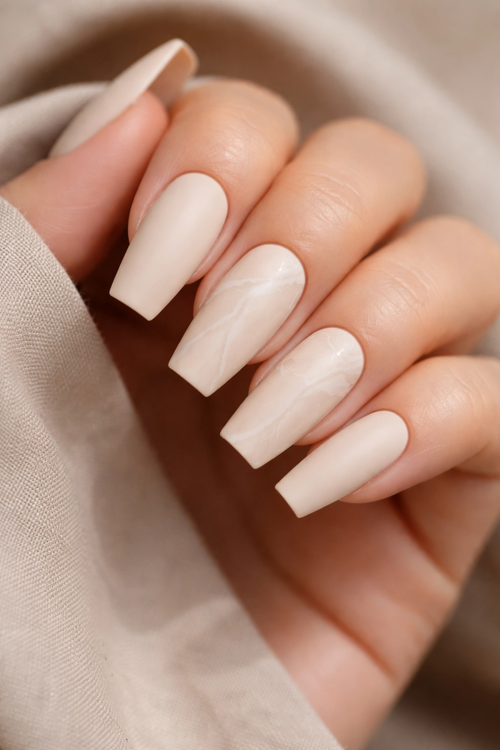 Oat milk matte nails with soft white marble veins on a neutral background.