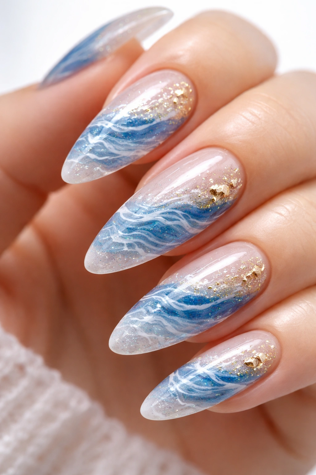 Close-up almond nail with blue white and clear gel wave textures and gold flecks