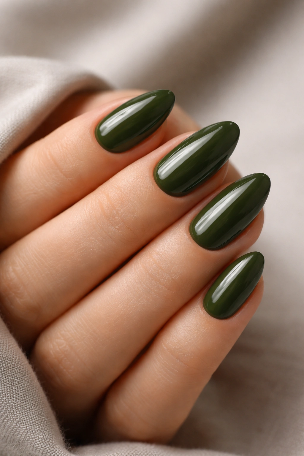 Close-up of short almond nails with deep olive green glossy polish and clean almond tips