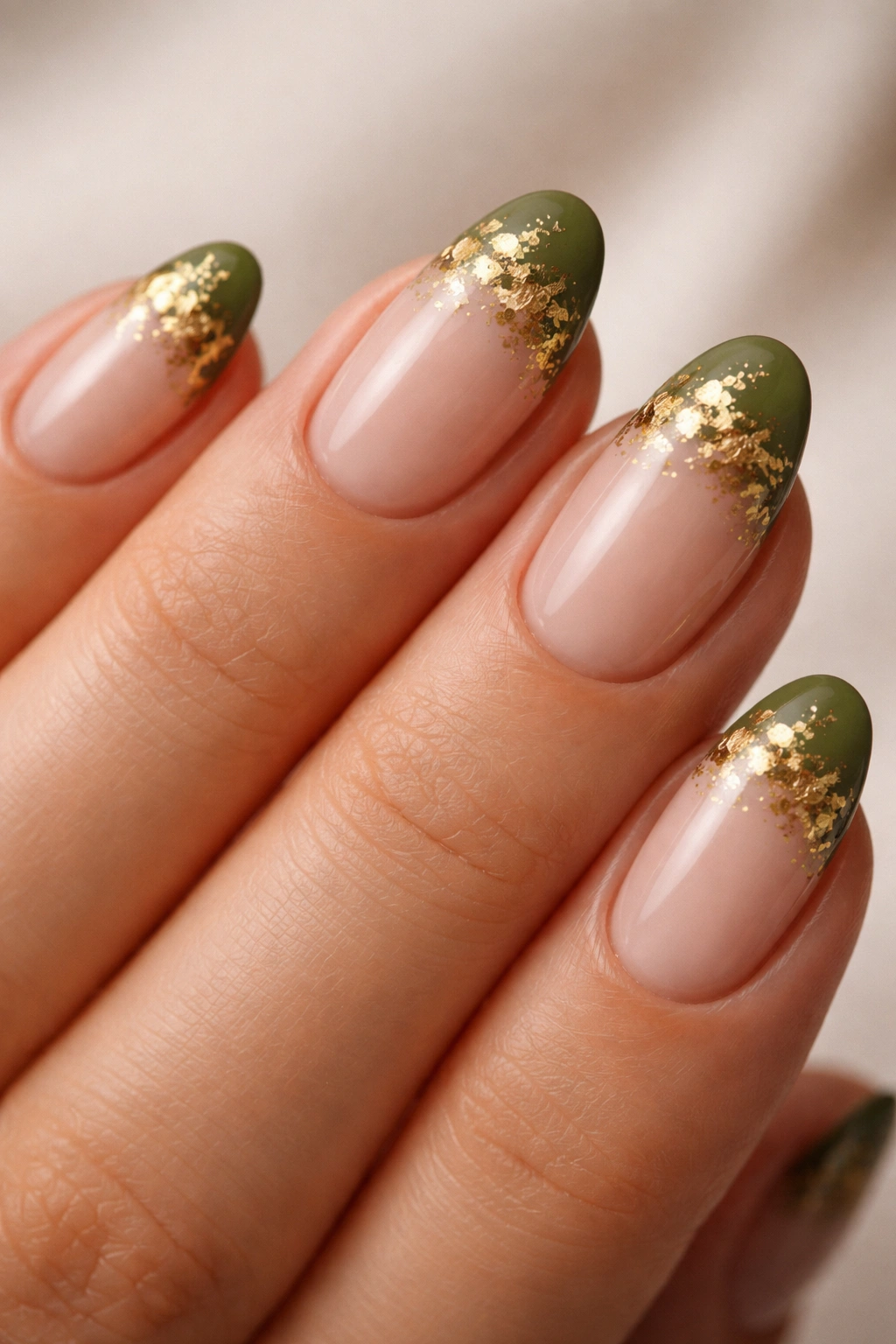 Close-up of short almond nails with olive green tips and gold foil accents