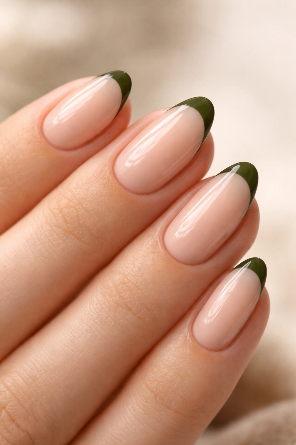 Close-up of nude almond nails with a slim olive micro-tip at the edge on a plain background