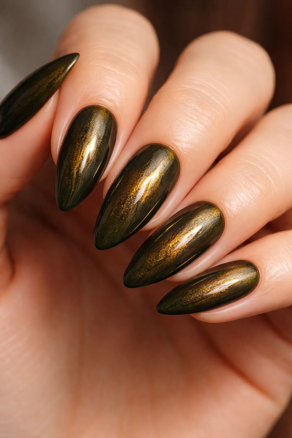 Close-up of almond nails in dark olive green with warm gold shimmer