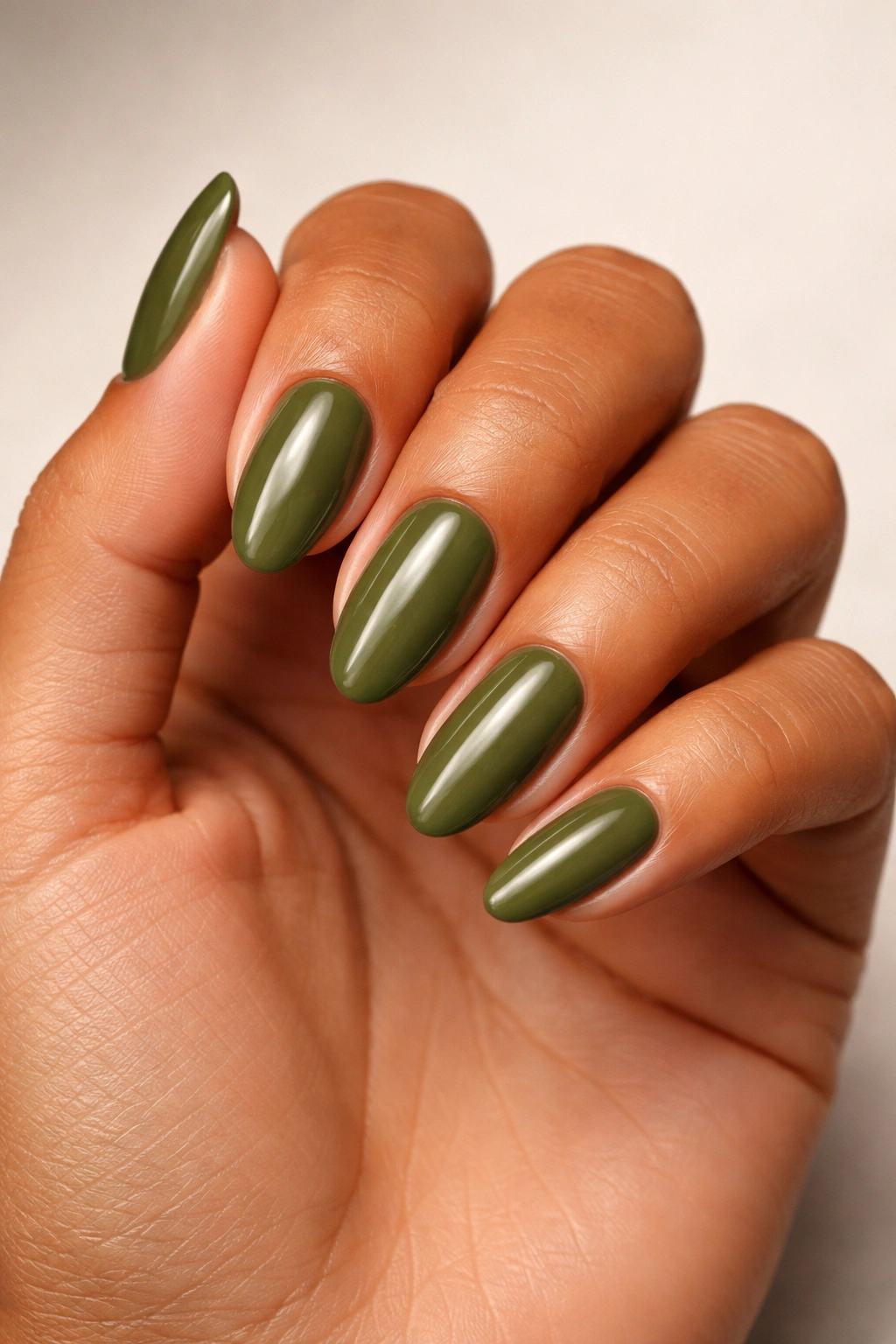 Close-up of a tanned hand with olive green nail polish.