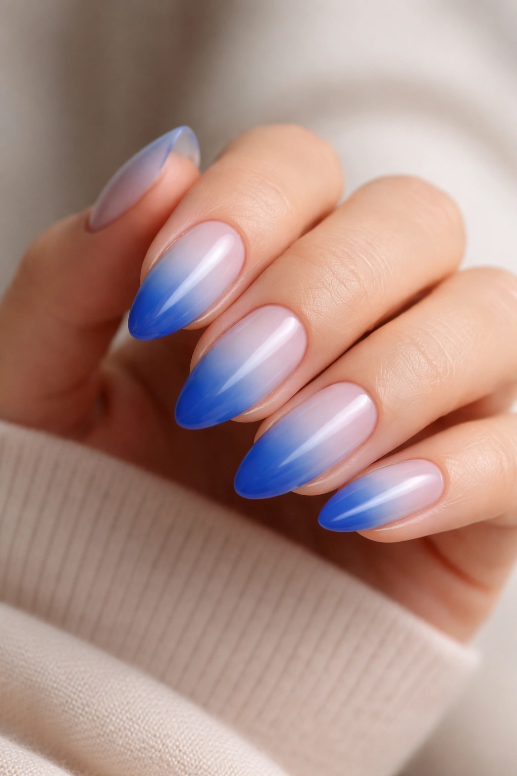 Close-up of ombre blue almond nails fading from light to dark on a sheer milky base.