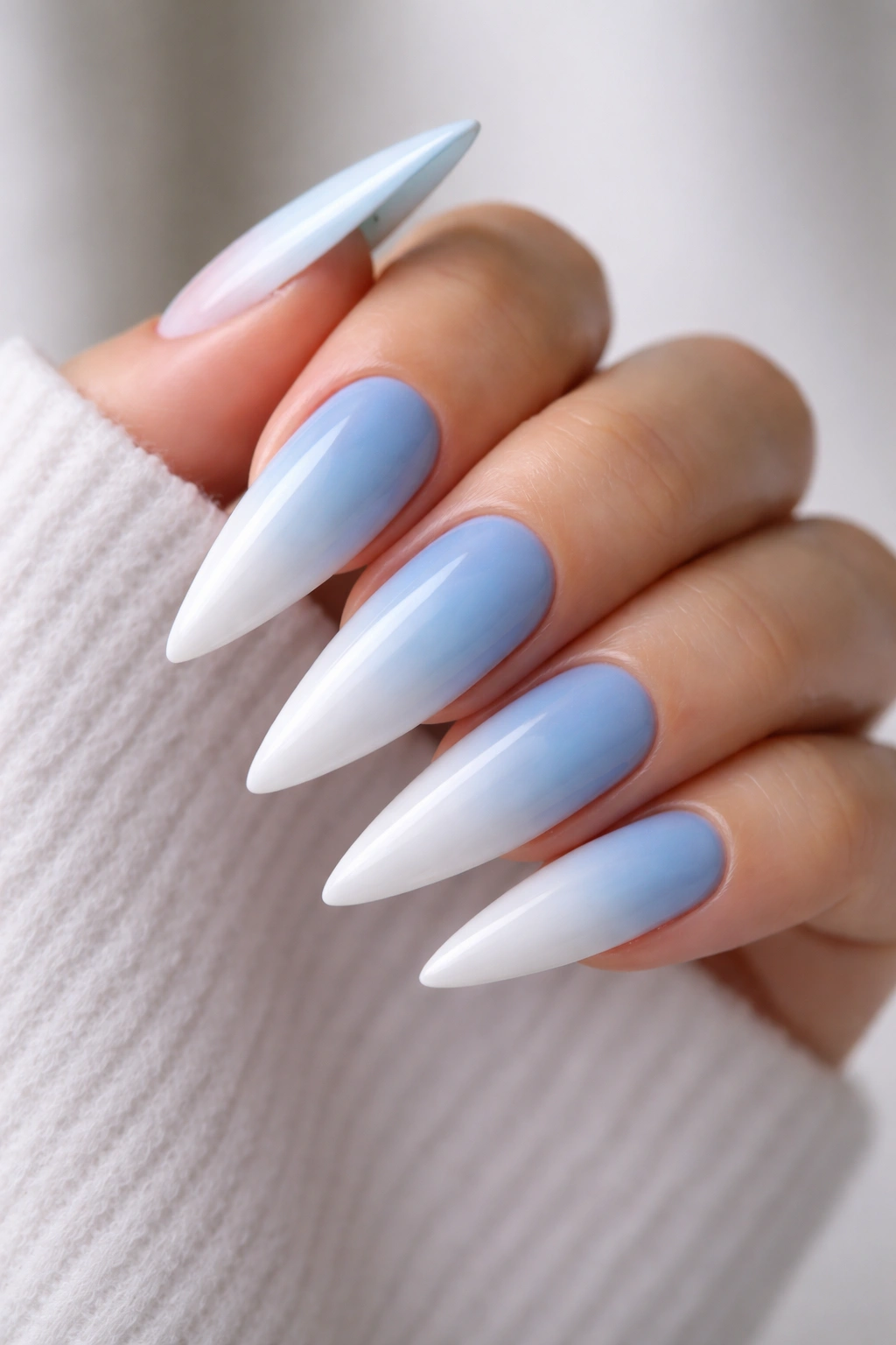 Close-up of ombré baby blue to white stiletto nails on a hand.