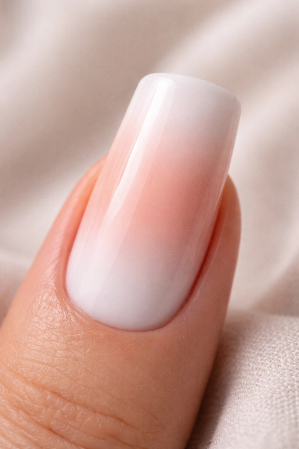 Close-up of a duck nail with a soft peachy-blush to white ombre gradient on a glossy finish