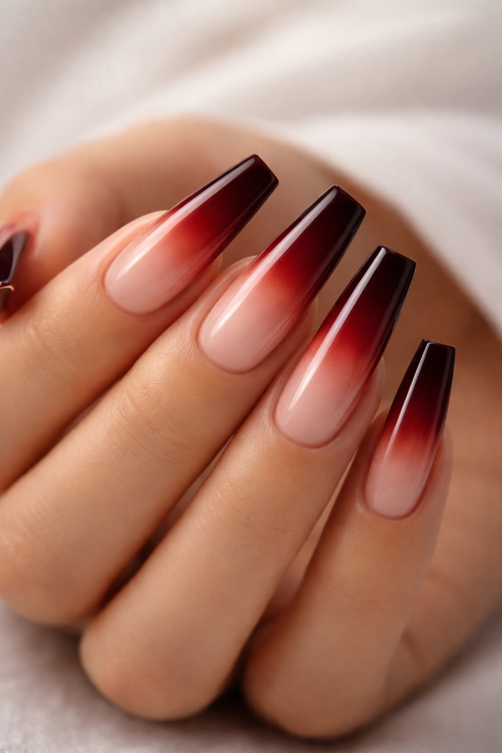 Close-up ombré nails blending nude base into burgundy tips.
