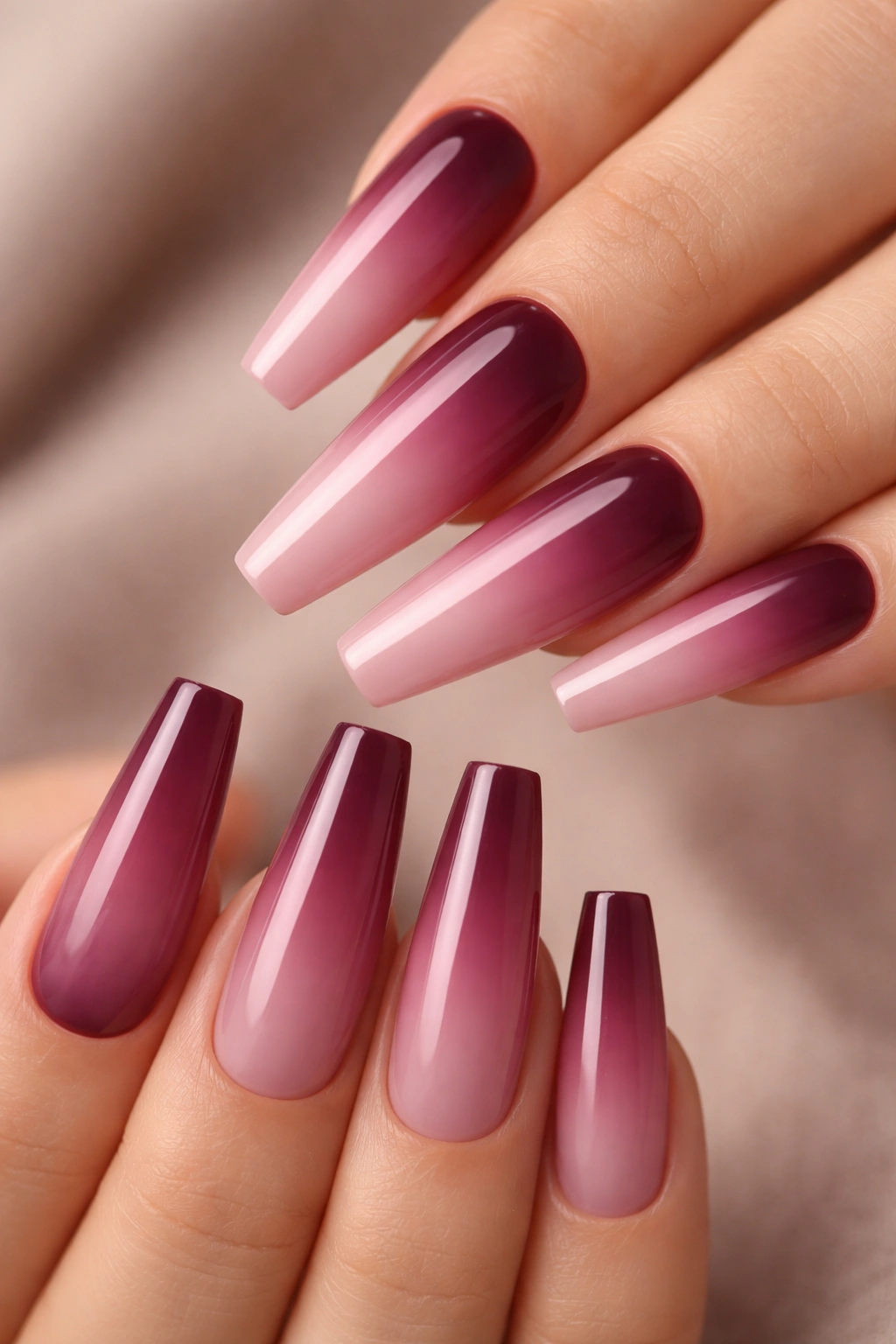 Close-up of coffin nails with burgundy to pink ombre gradient on a neutral background
