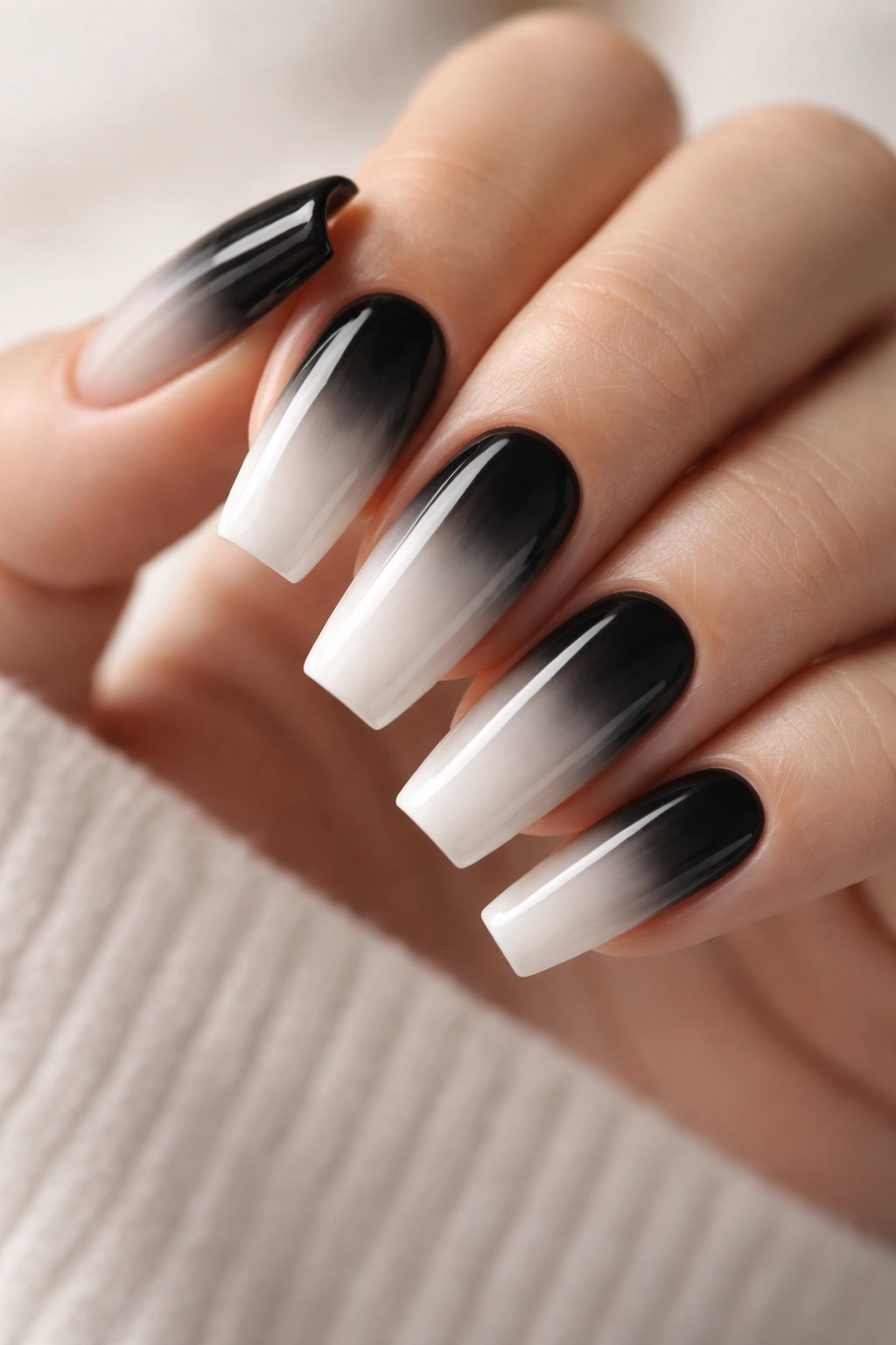 Close-up of coffin nails with a smooth black-to-white ombre gradient on a neutral background