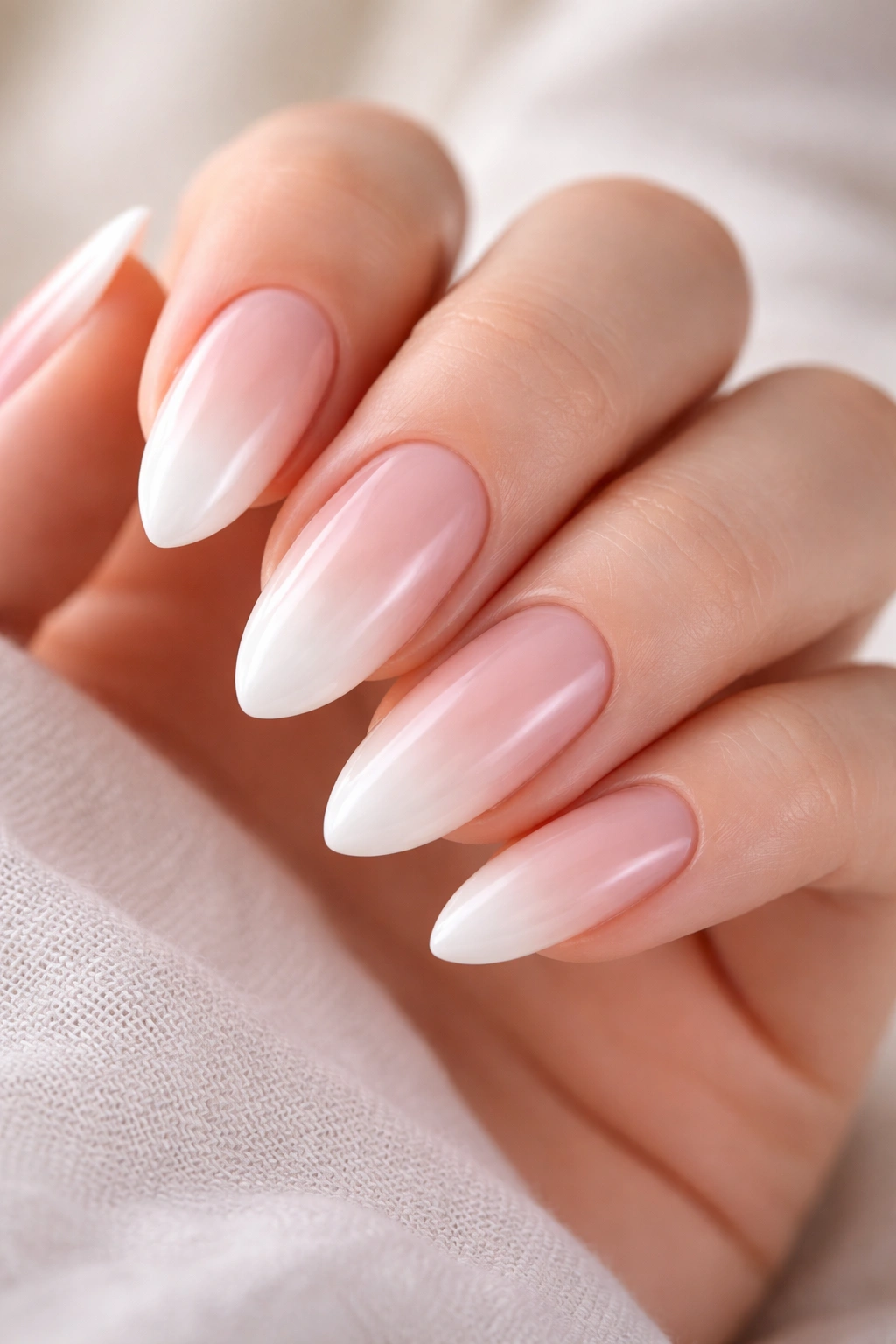Close-up of almond nails with a soft pink to white gradient