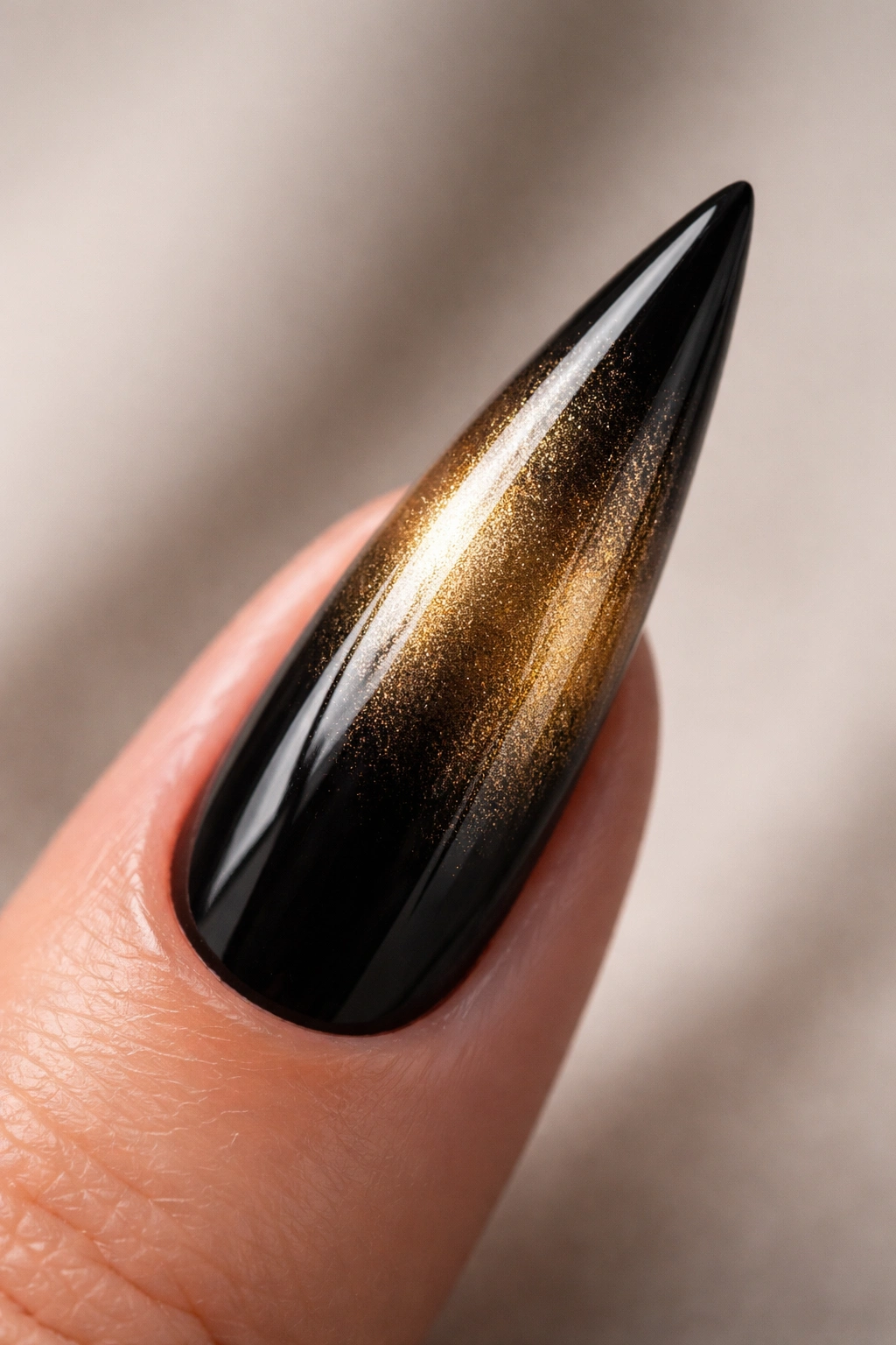 Black stiletto nail with gold ombre gradient on a dark base