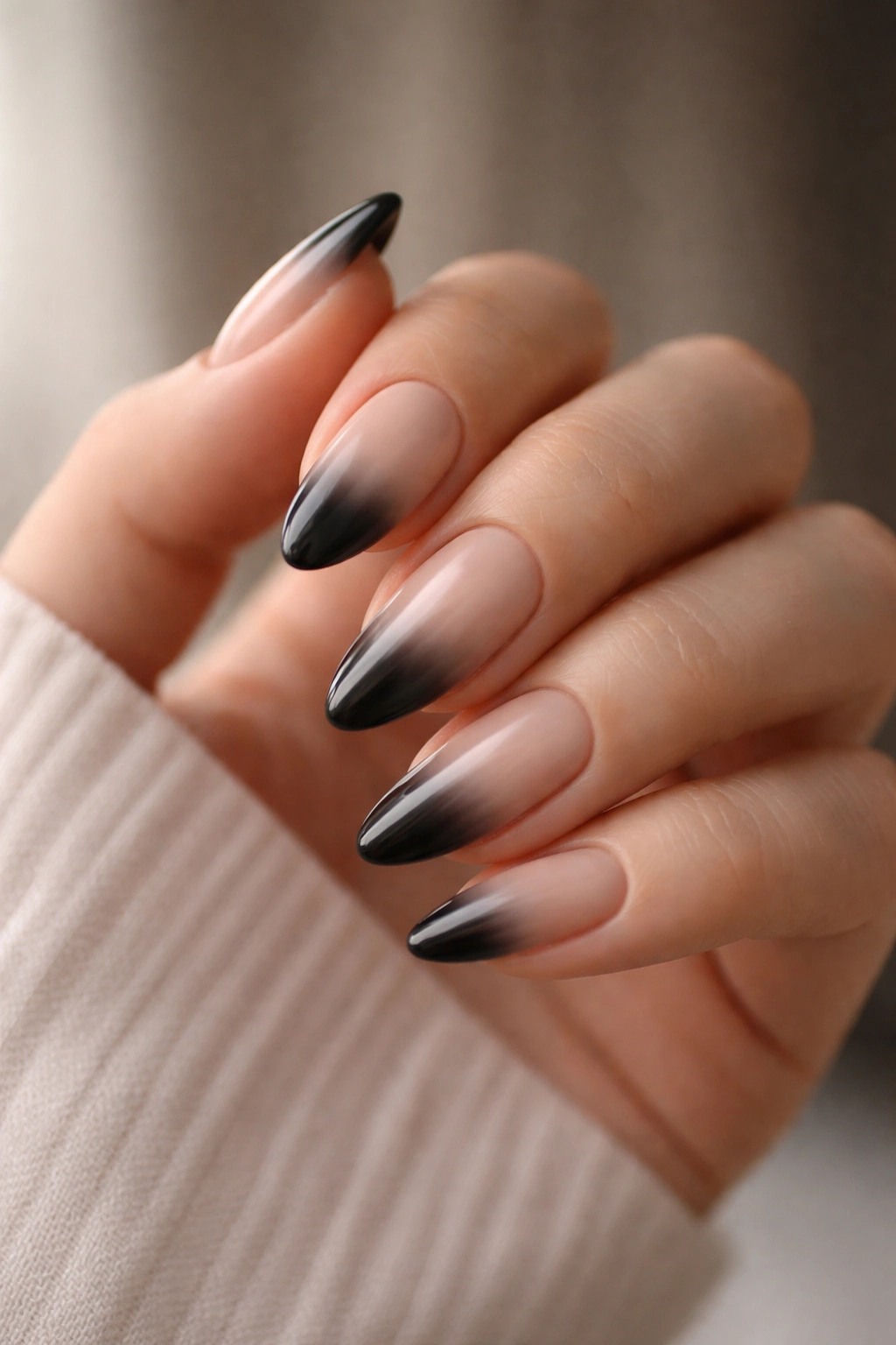 Close-up of almond nails with sheer nude base fading into smoky black tip on a hand